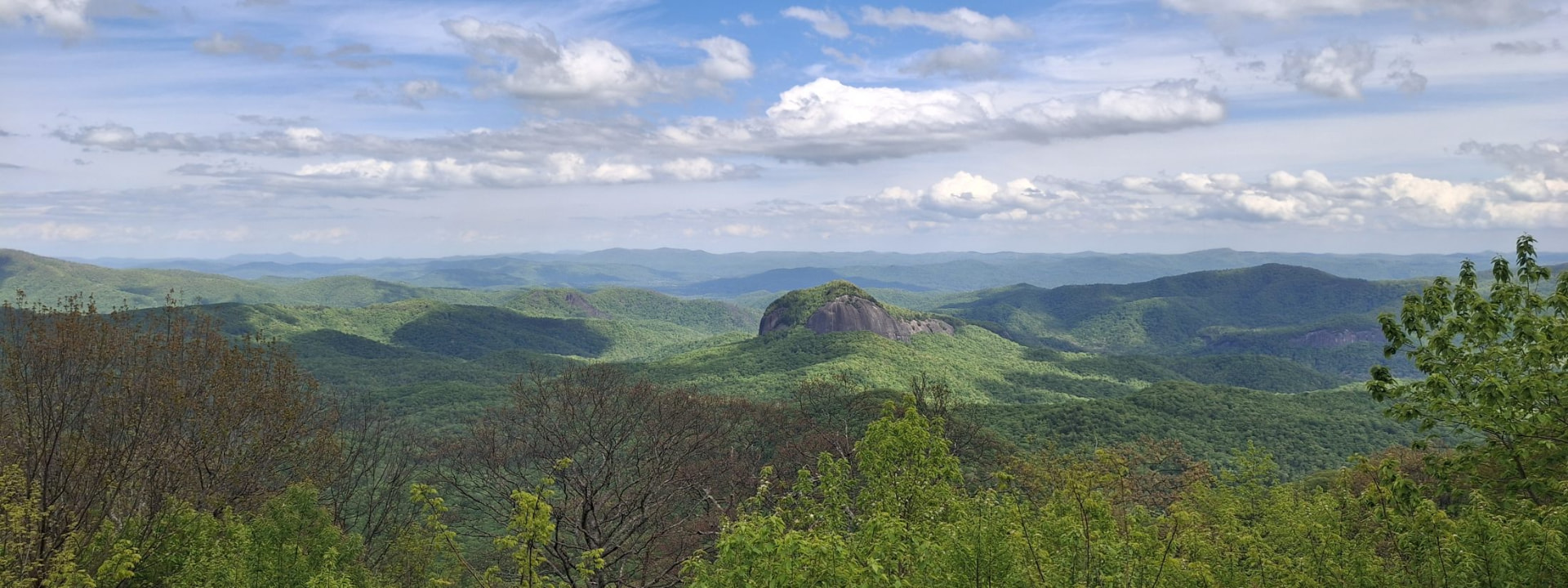 Looking Glass Rock rising above forested green ridges under a blue sky, seen from the Blue Ridge Parkway